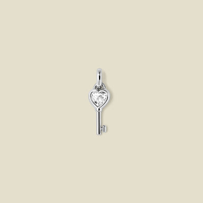 Silver key-shaped pendant with a heart shaped clear gemstone on a beige background