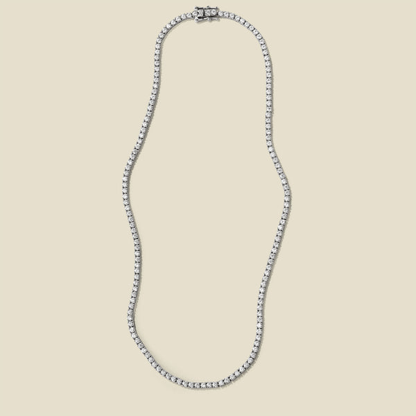 A silver prong-set tennis necklace, set against a solid beige background.