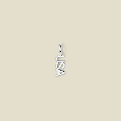 A small silver letter charm spelling 'USA' vertically, centered on a solid light beige background.