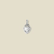 A small silver heart-shaped charm with a clear faceted heart-shaped gemstone, centered on a solid light beige background.