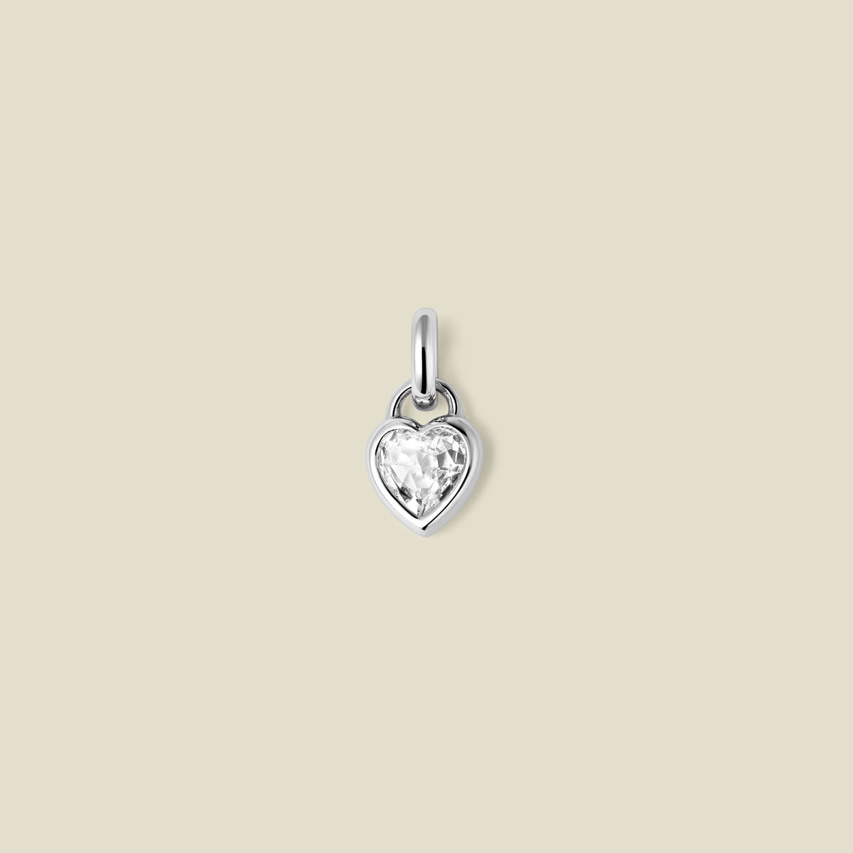 A small silver heart-shaped charm with a clear faceted heart-shaped gemstone, centered on a solid light beige background.