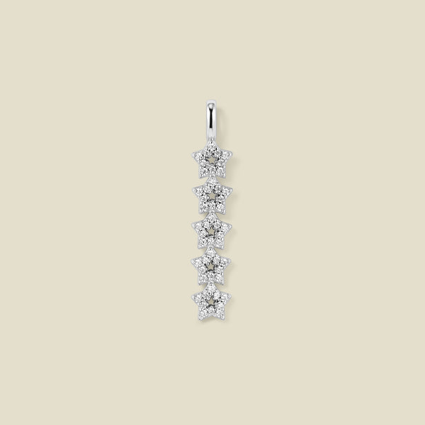 A silver pendant charm with five stars stacked vertically with clear stones, set against a solid beige background.