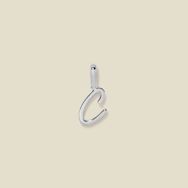 A polished silver initial pendant charm shaped like the letter 'C' in a cursive script, centered on a solid light beige background.