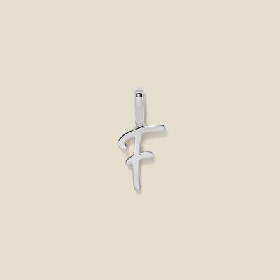 A polished silver initial pendant charm shaped like the letter 'F' in a cursive script, centered on a solid light beige background.