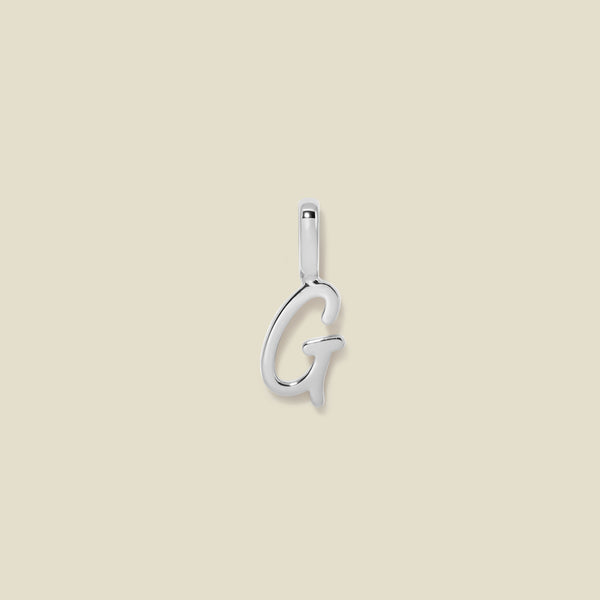 A polished silver initial pendant charm shaped like the letter 'G' in a cursive script, centered on a solid light beige background.