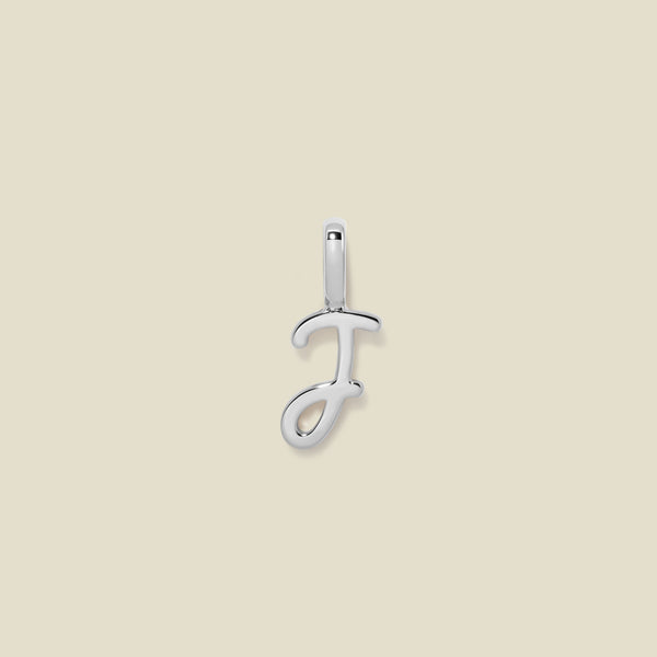 A polished silver initial pendant charm shaped like the letter 'J' in a cursive script, centered on a solid light beige background.