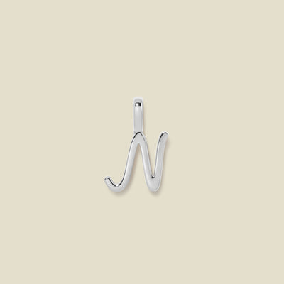 A polished silver initial pendant charm shaped like the letter 'N' in a cursive script, centered on a solid light beige background.
