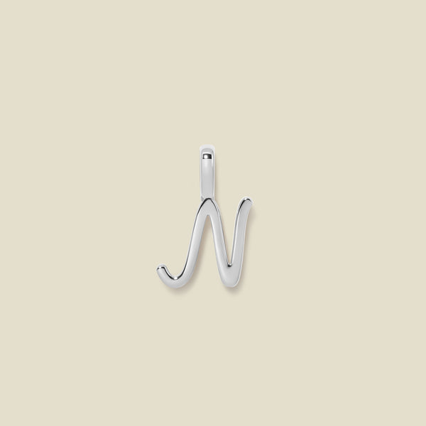 A polished silver initial pendant charm shaped like the letter 'N' in a cursive script, centered on a solid light beige background.