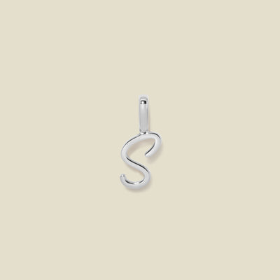 A polished silver initial pendant charm shaped like the letter 'S' in a cursive script, centered on a solid light beige background.