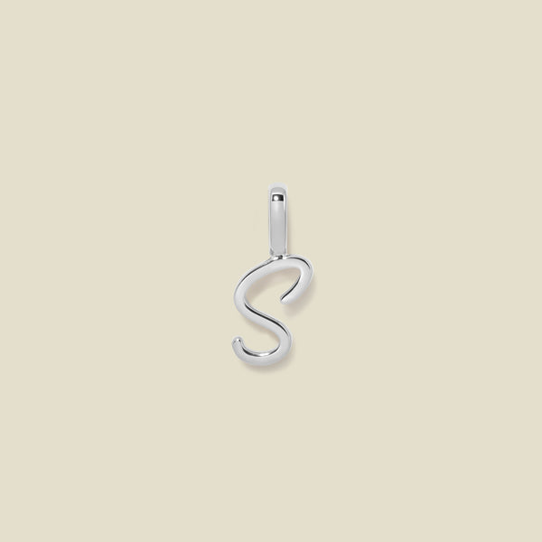 A polished silver initial pendant charm shaped like the letter 'S' in a cursive script, centered on a solid light beige background.