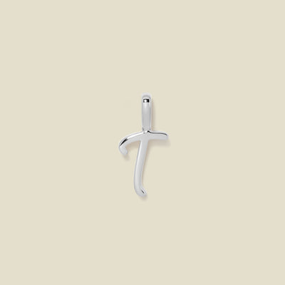 A polished silver initial pendant charm shaped like the letter 'T' in a cursive script, centered on a solid light beige background.