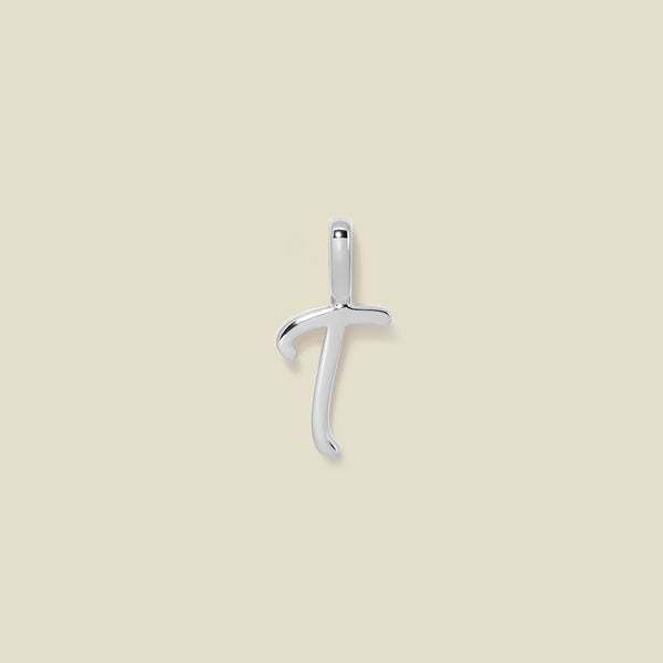 A polished silver initial pendant charm shaped like the letter 'T' in a cursive script, centered on a solid light beige background.