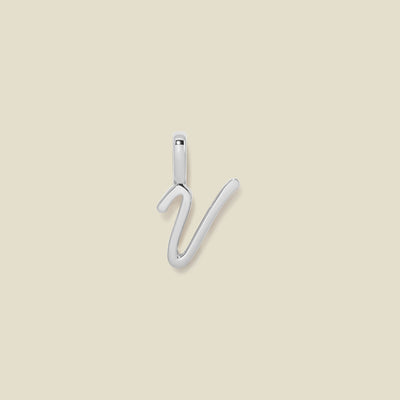 A polished silver initial pendant charm shaped like the letter 'V' in a cursive script, centered on a solid light beige background.