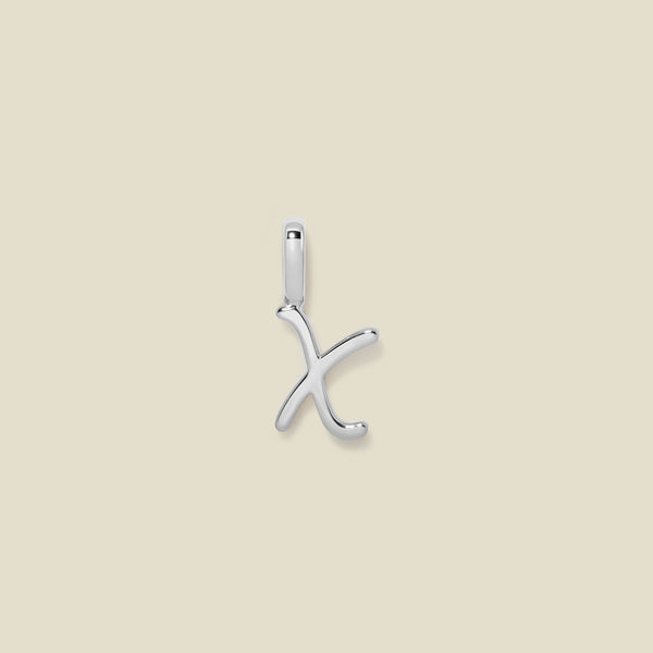 A polished silver initial pendant charm shaped like the letter 'X' in a cursive script, centered on a solid light beige background.