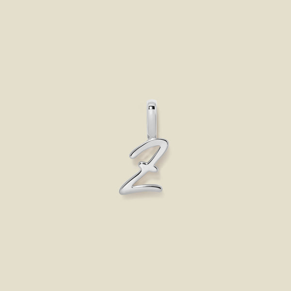 A polished silver initial pendant charm shaped like the letter 'Z' in a cursive script, centered on a solid light beige background.