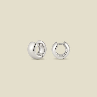 A pair of wide, polished silver hoop earrings standing up right at two different angles, set against a solid beige background.