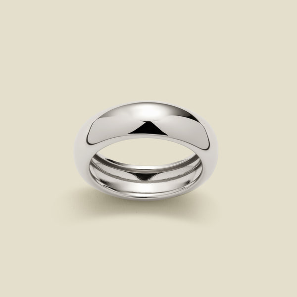 A wide, chunky polished silver ring set against a solid beige background.