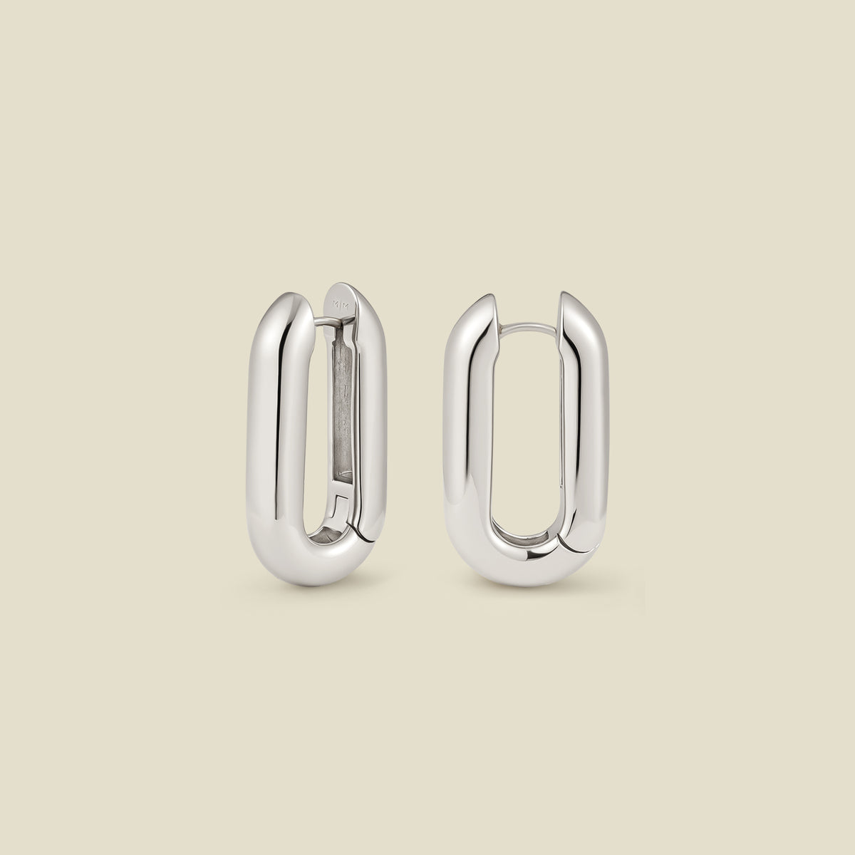 A pair of wide, polished silver paperclip shaped earrings standing up right and shown at two different angles, set against a solid beige background.