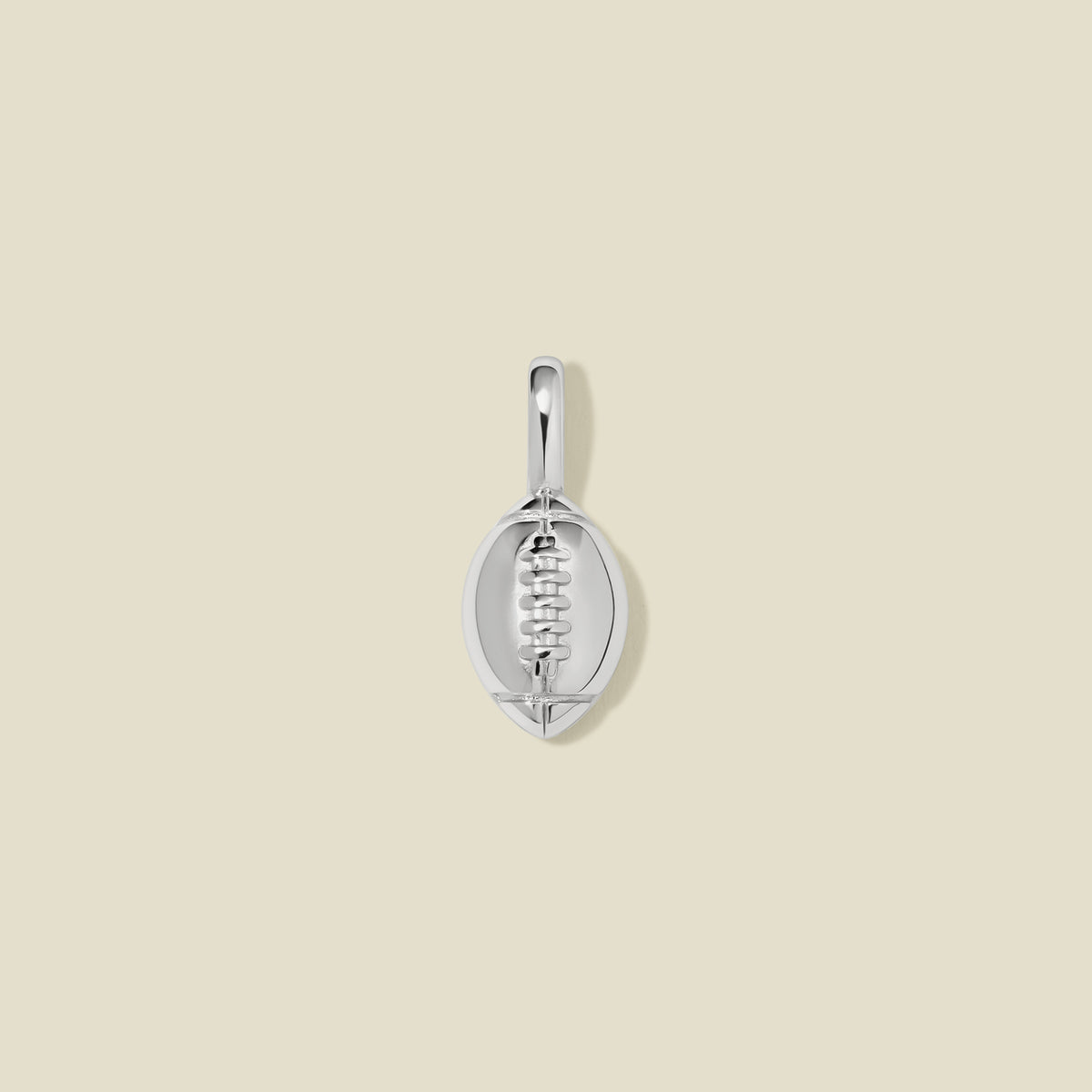 A silver football shaped charm with seam details, set against a solid beige background.