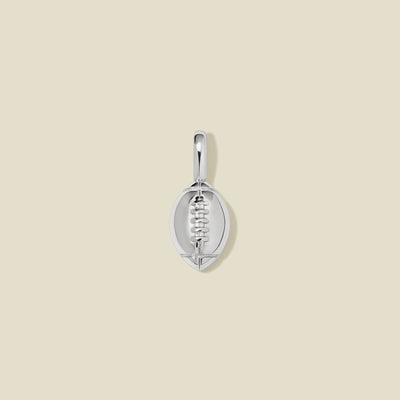 A silver football shaped charm with seam details, set against a solid beige background.