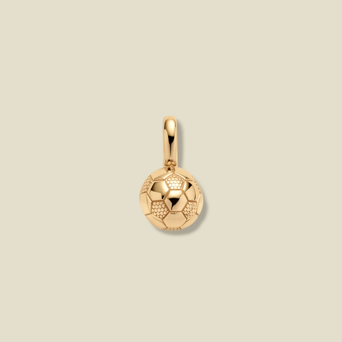 A small gold soccer ball charm pendant with a textured pattern, shown on a solid light beige background.