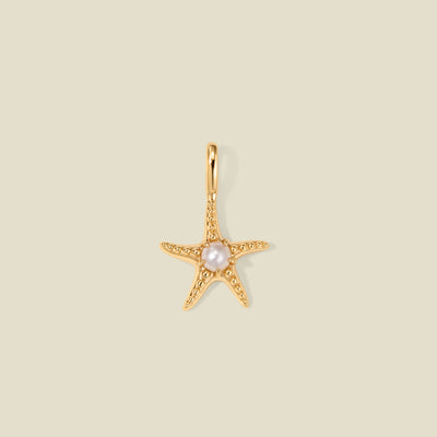 Gold starfish pendant charm with a pearl in the center on a beige background
