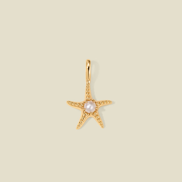 Gold starfish pendant charm with a pearl in the center on a beige background