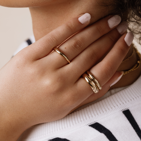 A close-up image of a hand resting on a person's neck wearing three polished gold rings in varying widths.