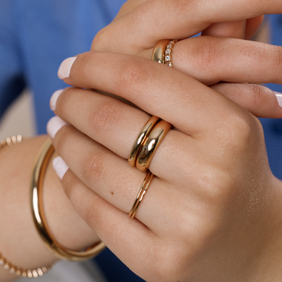 A close-up of a person's hands wearing multiple gold stacked rings in varying widths.
