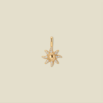 Gold sun-shaped pendant with clear gemstones on a beige background
