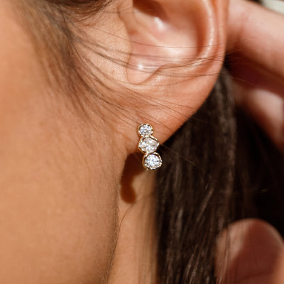 Close up of a person wearing a gold stud earring with three oval gemstones placed vertically 