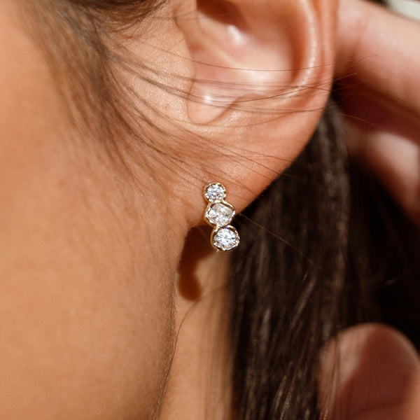 Close up of a person wearing a gold stud earring with three oval gemstones placed vertically 