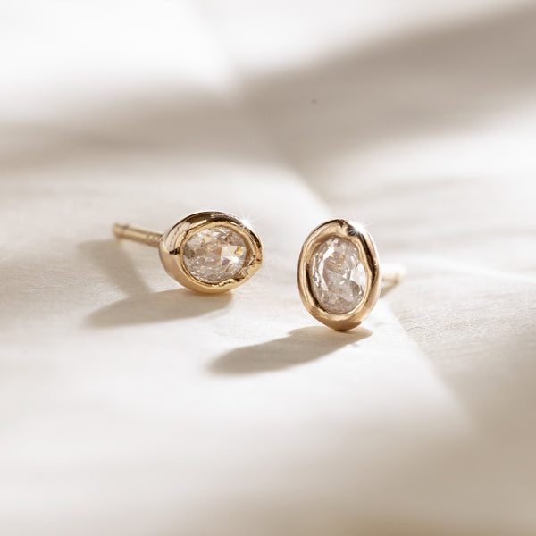 Gold bezel-set stud earrings with clear oval gemstones on a light background