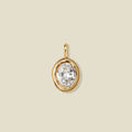 A large gold bezel-set clear oval gemstone, set against a solid beige background.