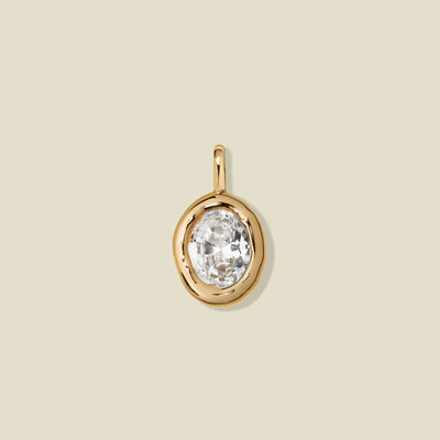 A large gold bezel-set clear oval gemstone, set against a solid beige background.