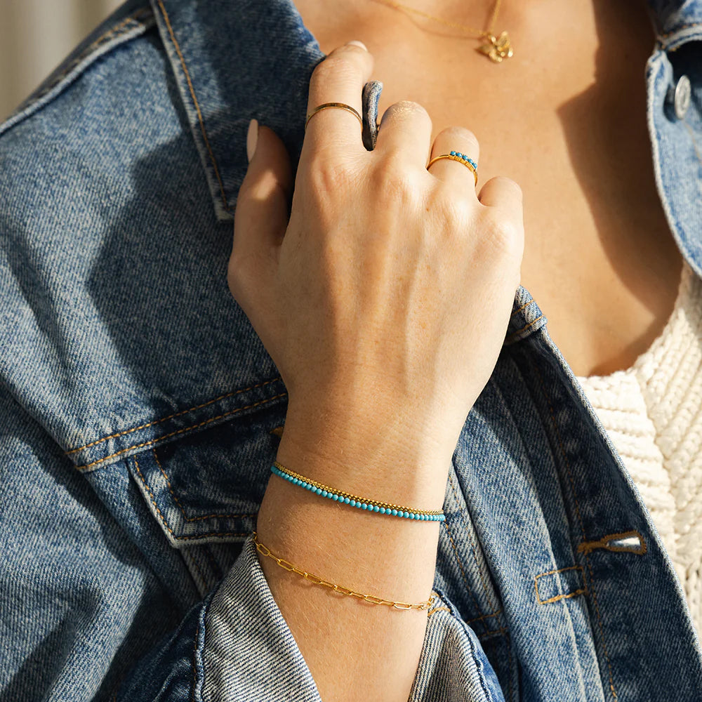 A womans wrist wearing multiple rings and bracelets, including a turquoise bracelet and gold and turquoise ring.