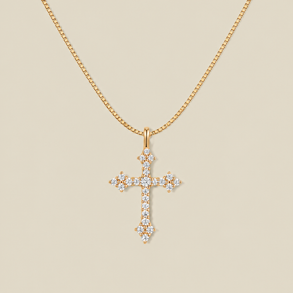 Gold cross pendant necklace with clear stones over the face on a beige background.