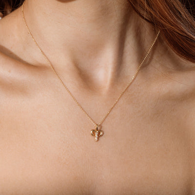 Close-up of a person wearing a delicate gold chain pendant necklace with a Aries zodiac symbol charm pendant.