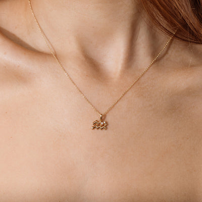 Close-up of a person wearing a delicate gold chain pendant necklace with an Aquarius zodiac symbol charm pendant.