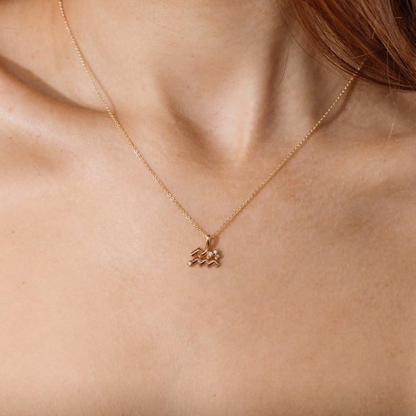Close-up of a person wearing a delicate gold chain pendant necklace with an Aquarius zodiac symbol charm pendant.