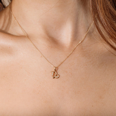 Close-up of a person wearing a delicate gold chain pendant necklace with a Capricorn zodiac symbol charm pendant.