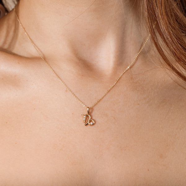 Close-up of a person wearing a delicate gold chain pendant necklace with a Capricorn zodiac symbol charm pendant.