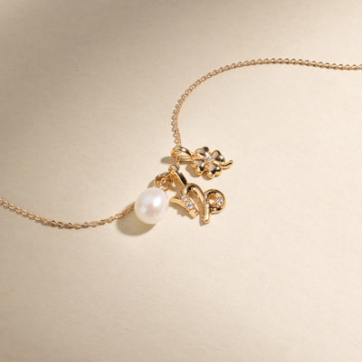 A gold chain necklace with a round pearl charm, a Capricorn zodiac symbol charm with clear accent stones, and a four leaf clover charm with one clear stone in the center.