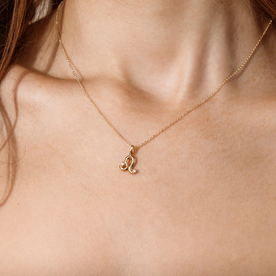 Close-up of a person wearing a delicate gold chain pendant necklace with a Leo zodiac symbol charm pendant.