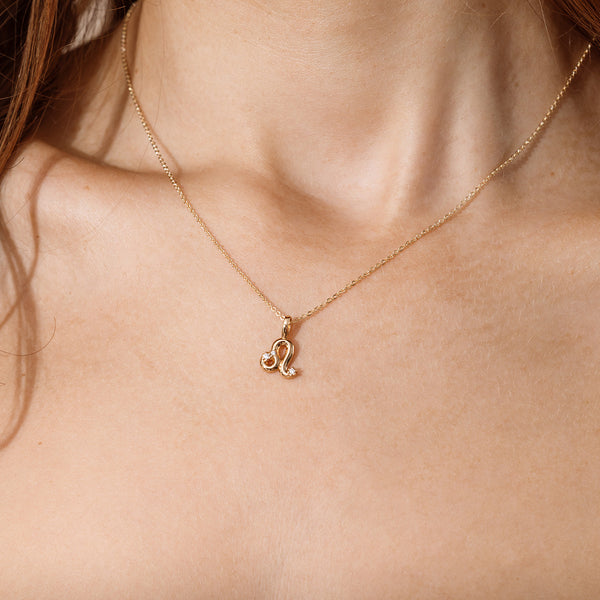 Close-up of a person wearing a delicate gold chain pendant necklace with a Leo zodiac symbol charm pendant.