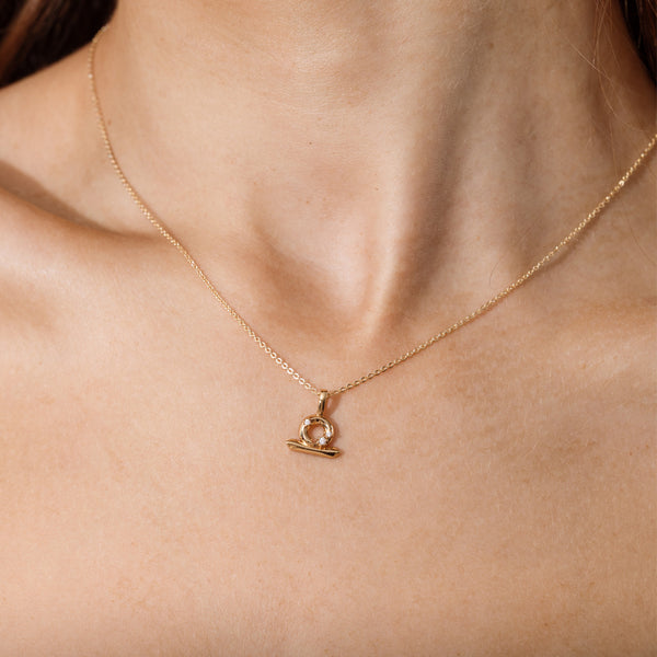 Close-up of a person wearing a delicate gold chain pendant necklace with a Libra zodiac symbol charm pendant.