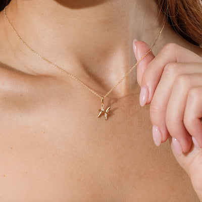 Close-up of a person wearing a delicate gold chain pendant necklace with a Pisces zodiac symbol charm pendant.