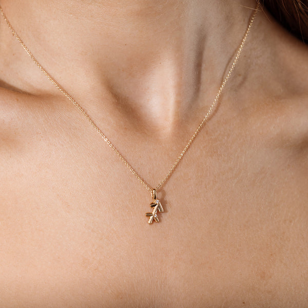 Close-up of a person wearing a delicate gold chain pendant necklace with a Sagittarius zodiac symbol charm pendant.