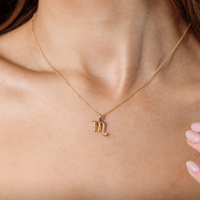 Close-up of a person wearing a delicate gold chain pendant necklace with a Scorpio zodiac symbol charm pendant.