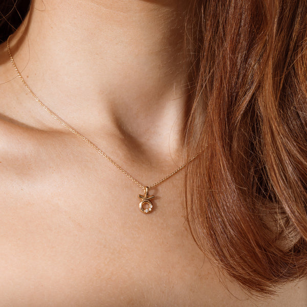 Close-up of a person wearing a delicate gold chain pendant necklace with a Taurus zodiac symbol charm pendant.